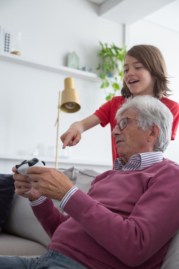 Elderly man and child playing video games together on a sofa, enjoying family time.